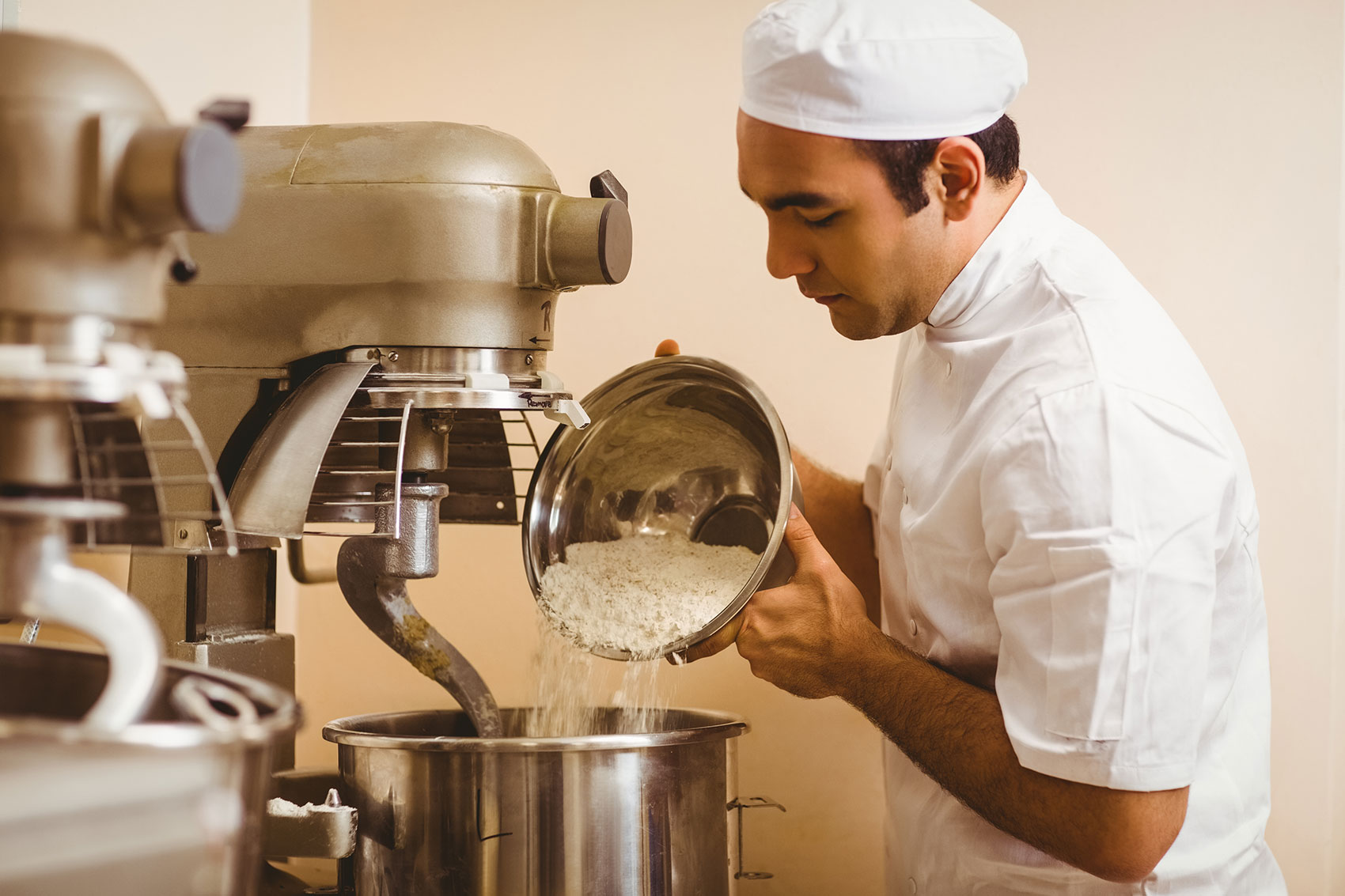 Baker pouring flour into large mixer